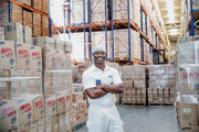 A smiling confectionery craftsman stands amidst boxes of packaged candy assortments in the Colombina Candy Confectionary Plant.